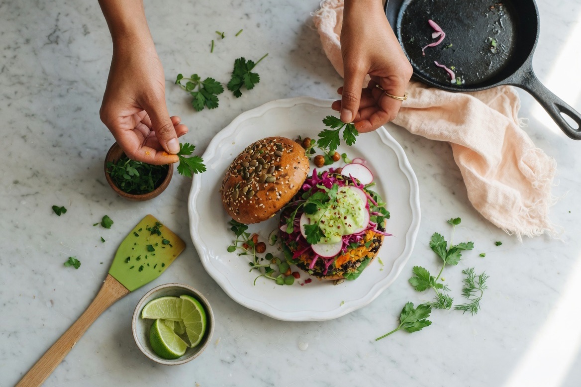 Overhead view of hands garnishing a plated black bean burger — promoting a recipe blog post on Pinterest
